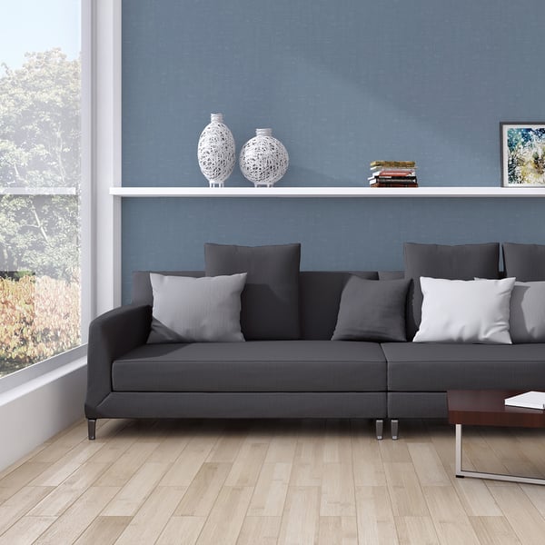 Dark gray sectional sofa with gray and white cushions on light wood floor, blue wall, shelf with ceramic vases and books