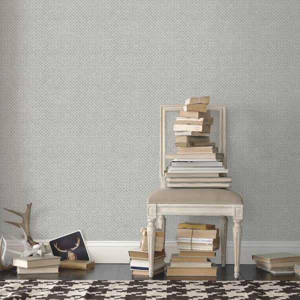 Silver grey diamond-plate wallpaper on the wall; in the foreground, a cream wooden chair with beige books and antler decor.