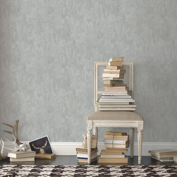 Distressed silver-grey wallpaper with a vintage, weathered texture on a wall in a muted gray room.