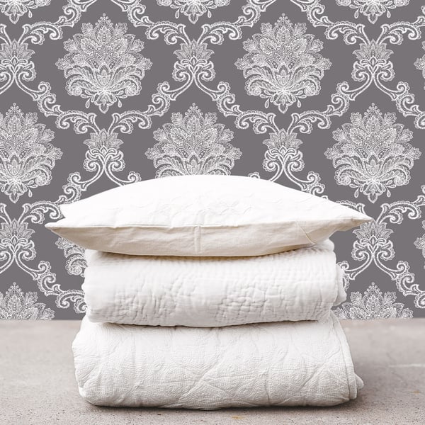 Stack of white pillows, a quilt, and a blanket against black damask wallpaper.