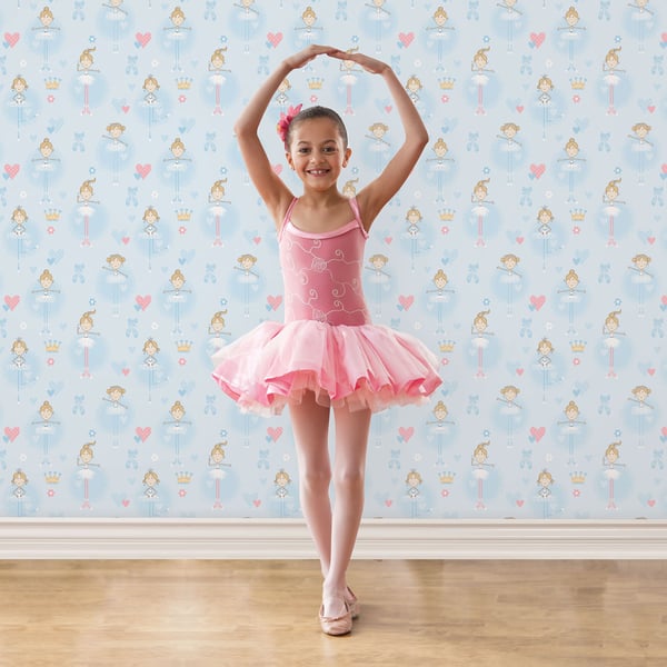 Child in pink ballet leotard and tulle tutu, pink slippers, arms raised in ballet pose on wooden floor.