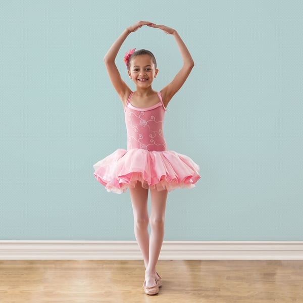 Pink ballet tutu with heart pattern, fluffy tulle skirt, light pink ballet shoes, girl with arms overhead against mint wall.
