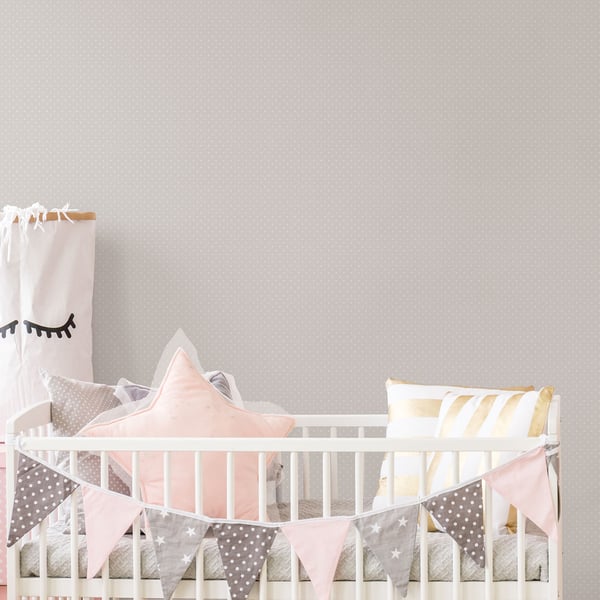 White metal baby crib with pastel pink star pillow, grey & yellow striped cushions, and pink bunting in a cozy nursery.