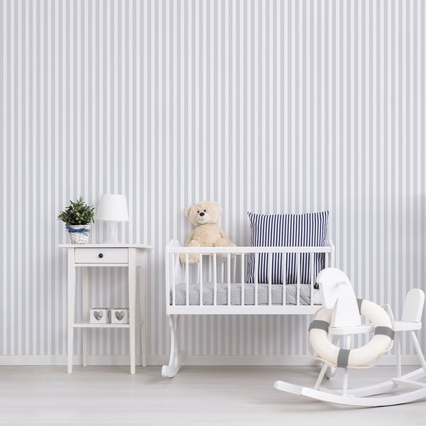 White baby crib with teddy bear and blue striped pillow, white side table with plant and lamp, rocking chair, striped walls.
