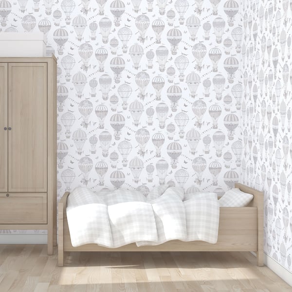 Light wood toddler bed with white-gray plaid blanket and pillow beside a matching wooden wardrobe; gray hot-air balloon wallpaper.