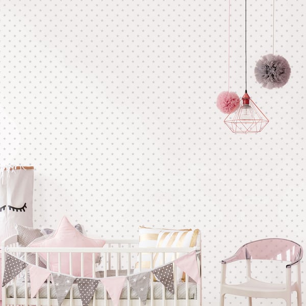 White wooden baby crib with pink bedding, pastel pennant banner, pink chair & geometric pendant lights in a polka-dot nursery.