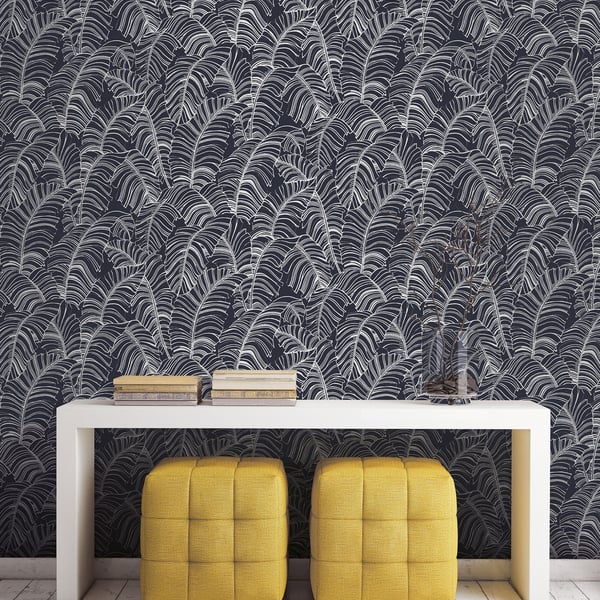 Dark palm-leaf wallpaper, white rectangular console table, and two yellow tufted cube ottomans beneath; books on top.
