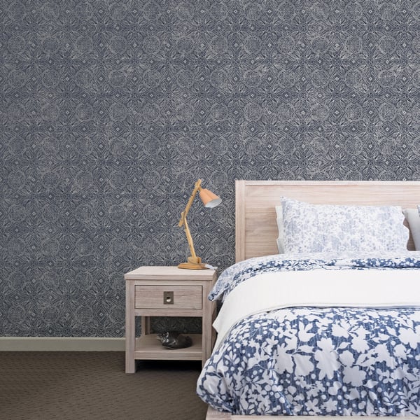 Bedroom with dark patterned wallpaper, light wood bed and nightstand, blue-and-white floral bedding, wooden bedside lamp.
