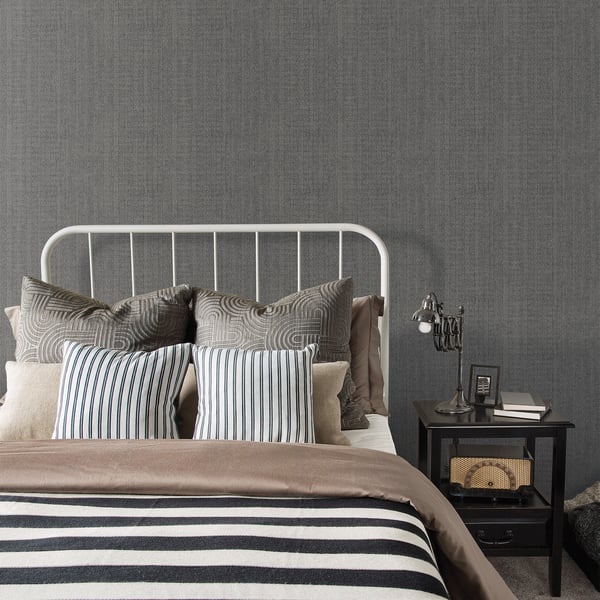 White metal bed frame with blue-gray striped pillows, taupe duvet, gray walls, and black nightstand with lamp.