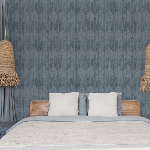 Boho bedroom with blue textured wallpaper, wooden bed frame, light gray blanket, cream pillows, & woven rope pendant lamps.