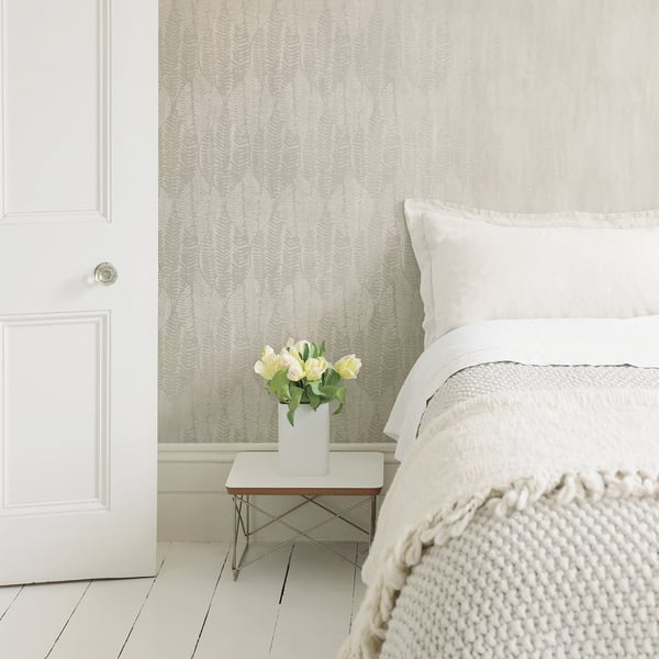 Soft white bedroom with a knitted cream throw on the bed, white pillows, a small white side table and a vase of pale roses.