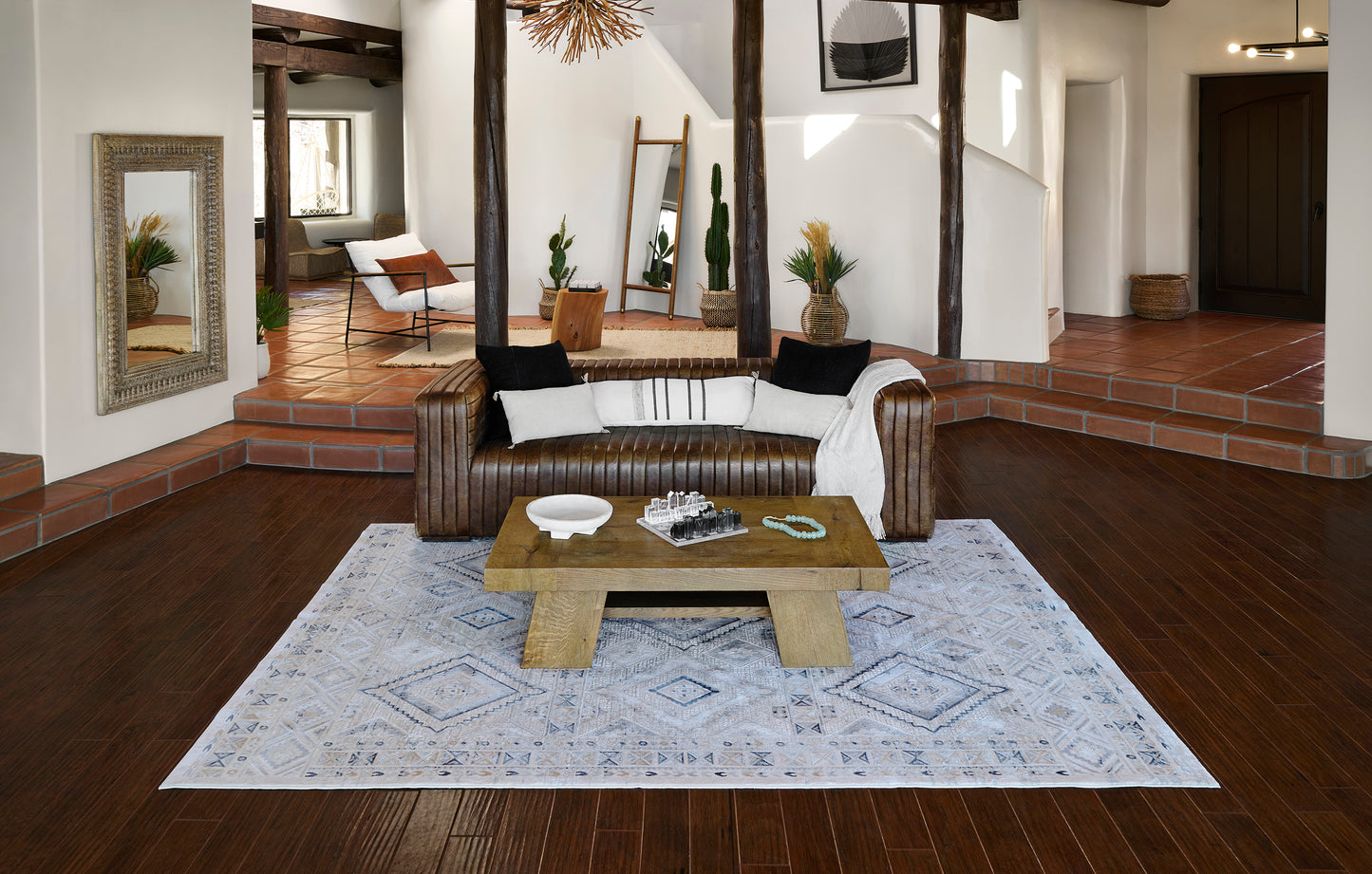 Brown leather sofa with white/black cushions, chunky wooden coffee table on a light blue geometric rug in a boho living room.
