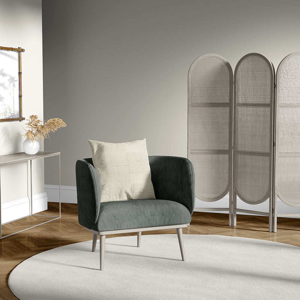 Dark sage-green upholstered armchair with a beige cushion in a modern living room, circular rug and woven room divider.