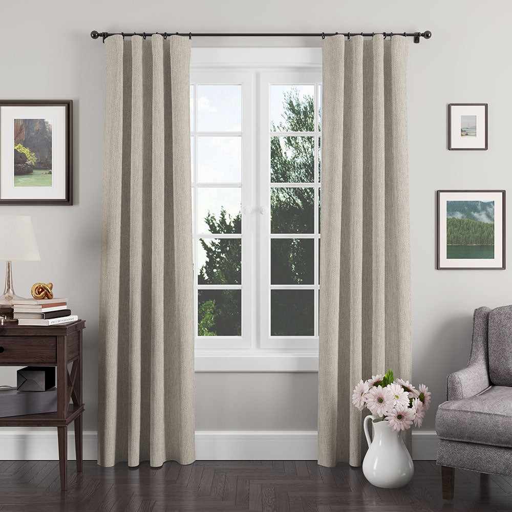 Beige textured panel curtains with rings on a black rod, framing a white window in a cozy living room.
