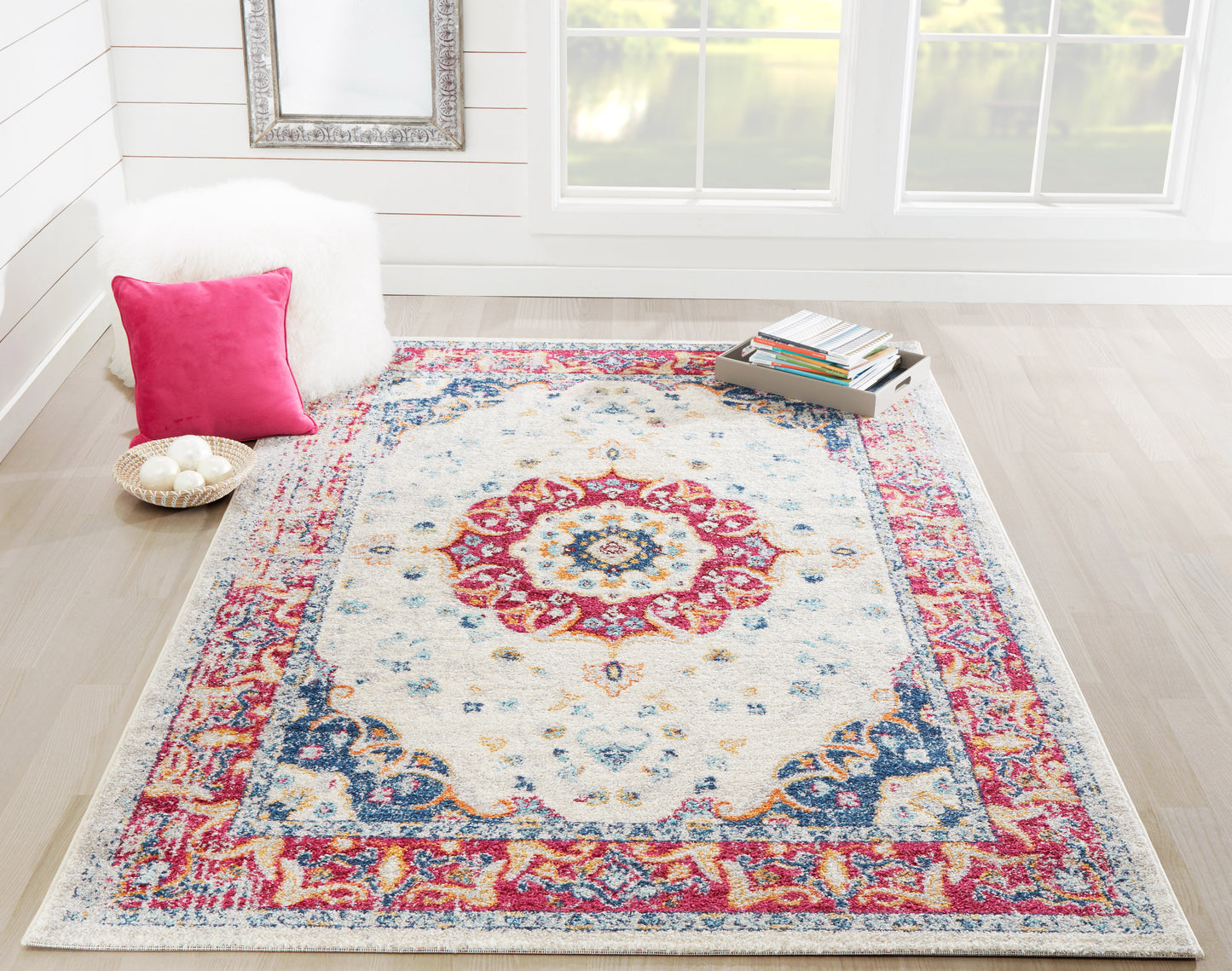 Oriental-style area rug with ivory field, rich red and blue border and central medallion in a bright cozy living room.