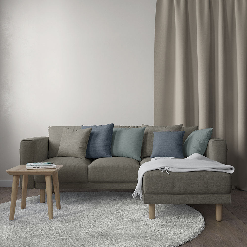 Taupe fabric sectional sofa with blue-gray cushions, round wooden coffee table, and a white throw in a neutral living room.