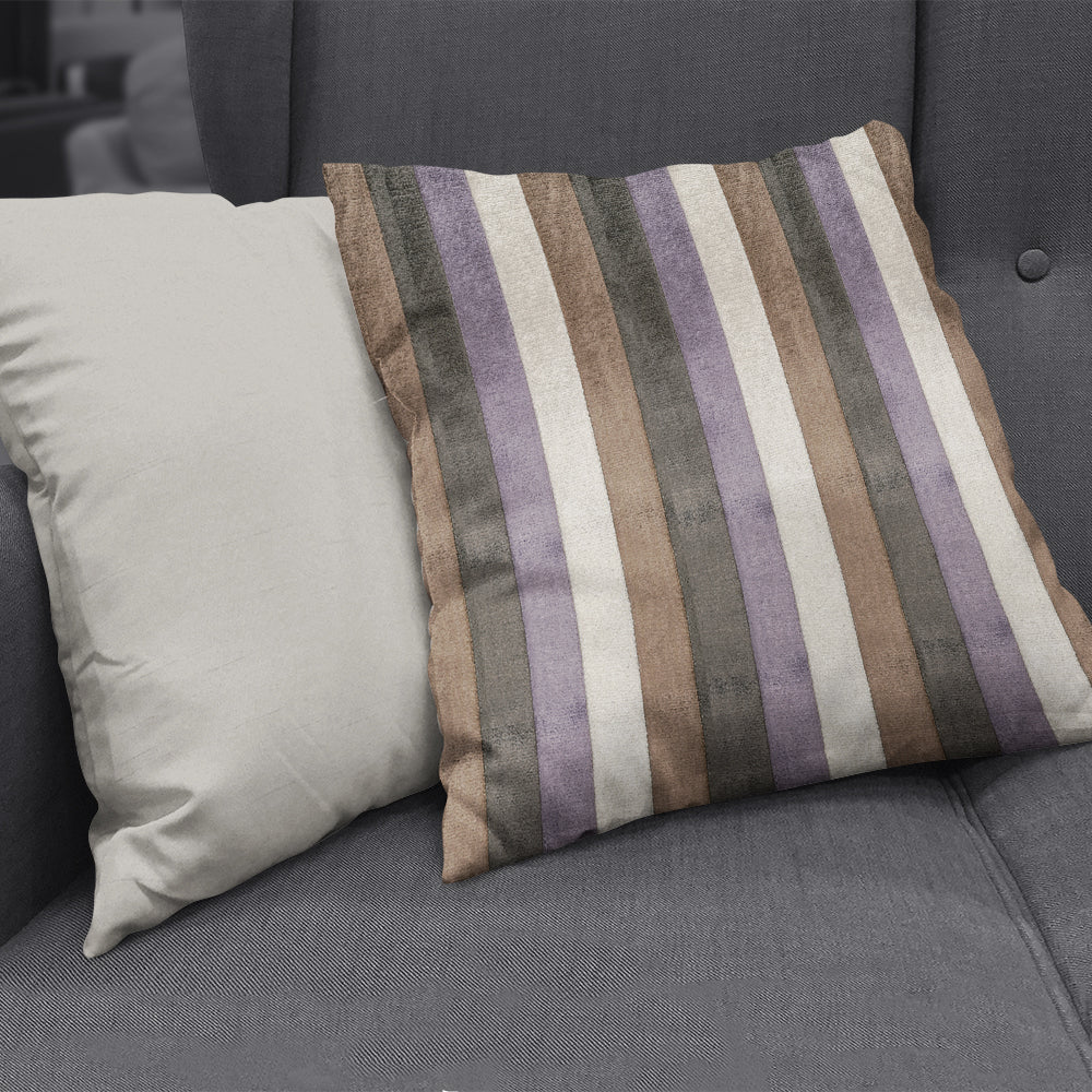 Two decorative pillows on a dark gray sofa; striped lavender, brown, taupe and cream pillow beside a plain beige pillow.