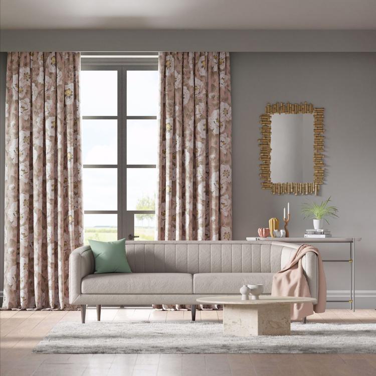 Pink floral curtains frame a gray tufted sofa in a modern living room with a marble coffee table and gold mirror.