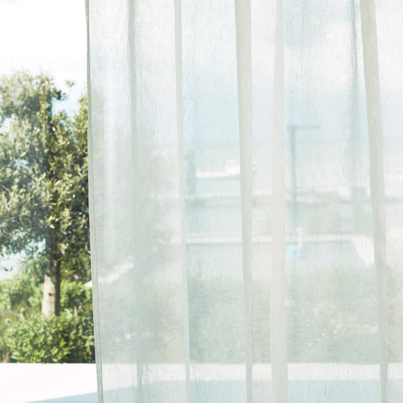 Sheer oyster curtain panels with soft vertical folds, outdoor view of greenery and a faint building beyond.