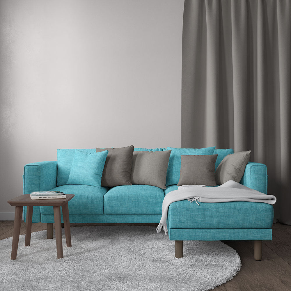 Teal fabric sectional sofa with chaise on right, grey cushions, light throw, wooden coffee table, grey rug and curtains.