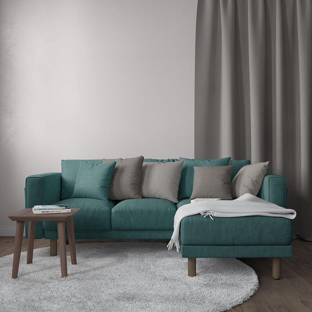Teal L-shaped sofa with gray and beige cushions, white throw, wooden legs, round gray rug and small wooden coffee table