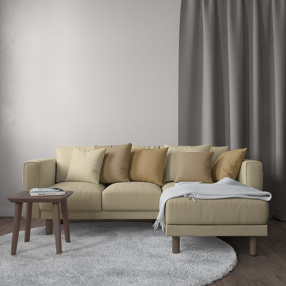 Beige fabric sectional sofa with chaise on the right & neutral cushions, gray rug, and round wooden side table with a throw.