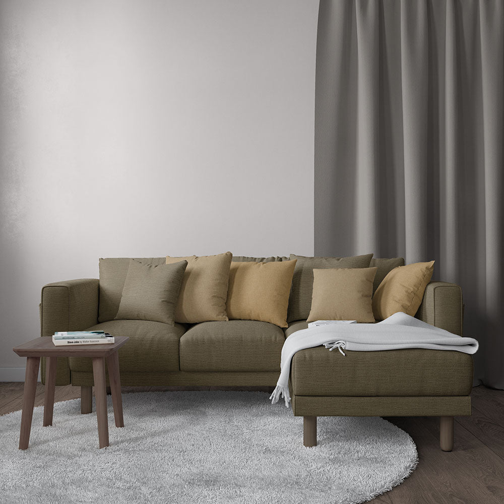 Olive-green sectional sofa with right chaise, beige cushions, white throw, wooden legs, beside a small wooden side table on a gray rug.