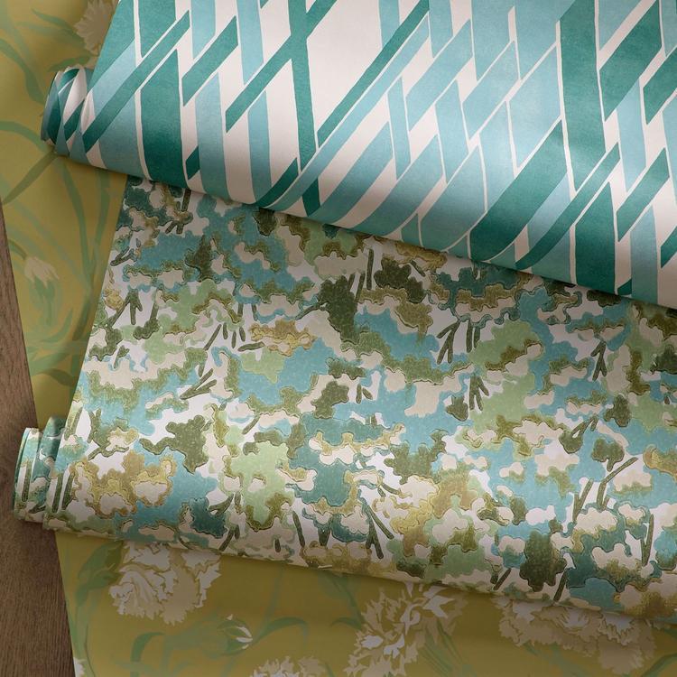 Three rolls of wallpaper with different patterns on a wooden surface.
