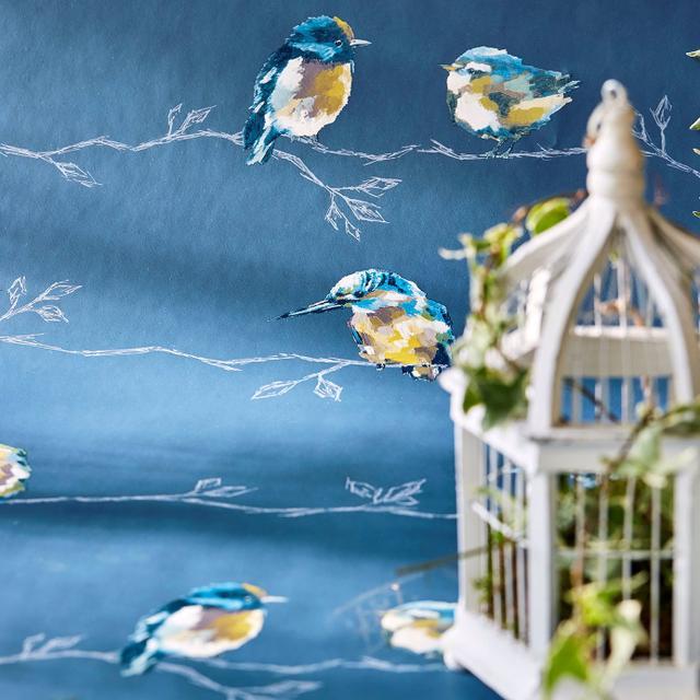 Blue wallpaper featuring hand-painted blue-and-yellow birds perched on white branches; foreground white birdcage with greenery.