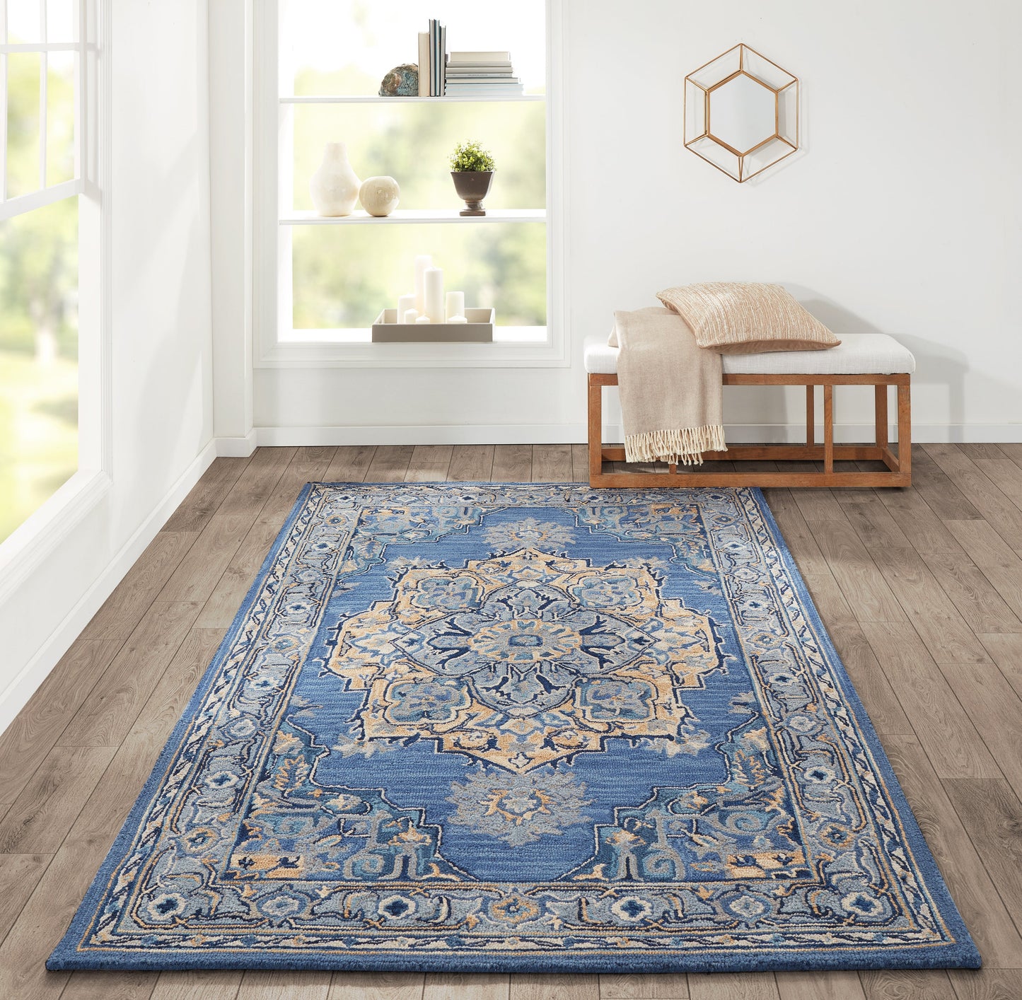 Blue ornate oriental area rug with cream and beige medallion pattern on wood floor beside a wooden bench.