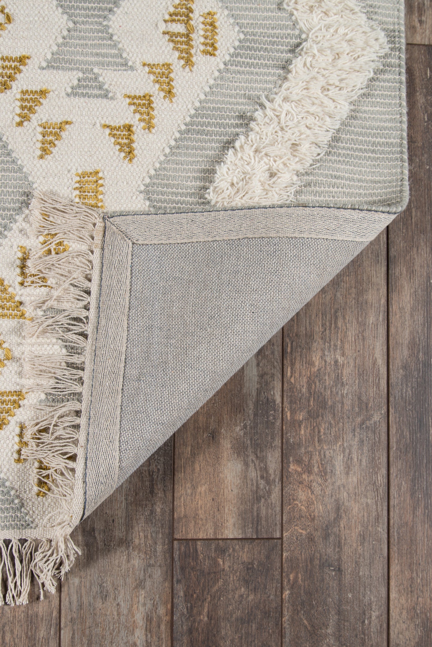 Gray geometric area rug with ivory and mustard accents, fringed edges, folded to show underside on wood floor.