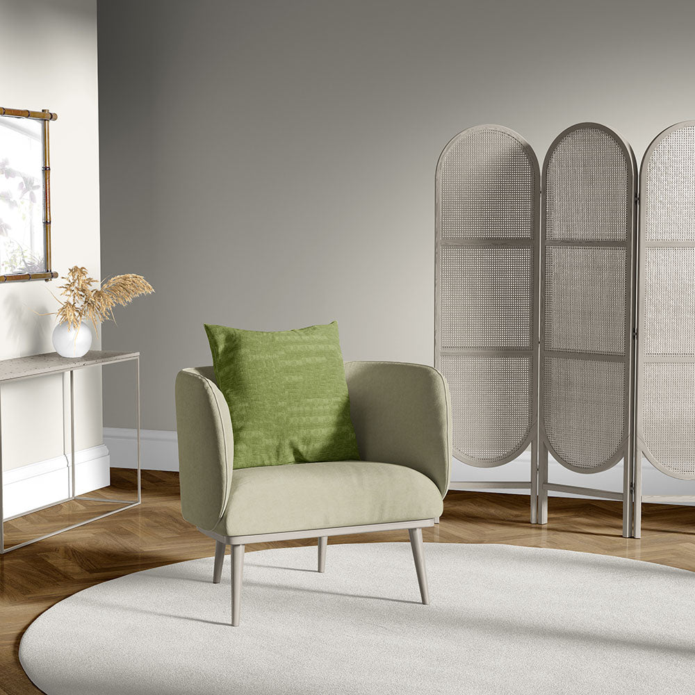 Olive fabric armchair with green cushion, light wood legs, against a grey folding screen and beige rug.
