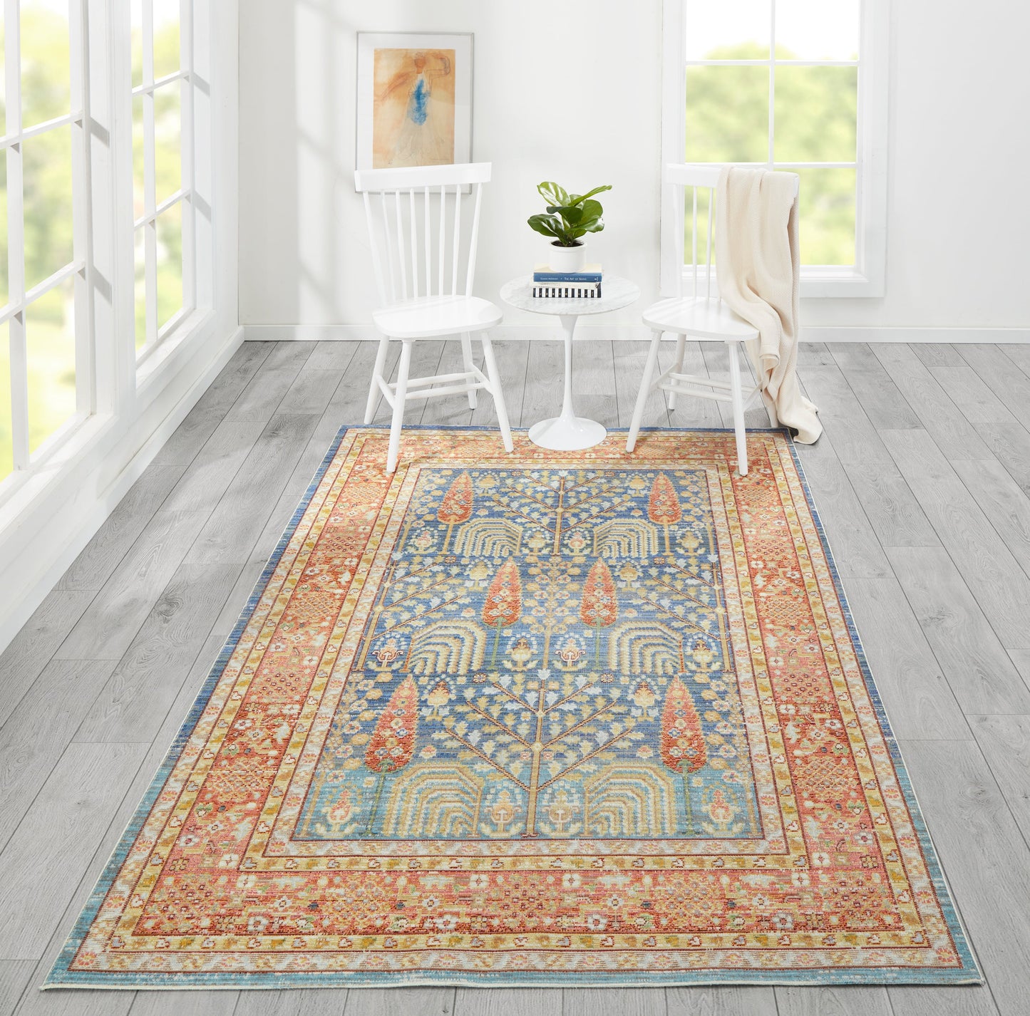 Rectangular oriental-style rug in blue, gold and coral with intricate border, in a white living room with two white chairs.