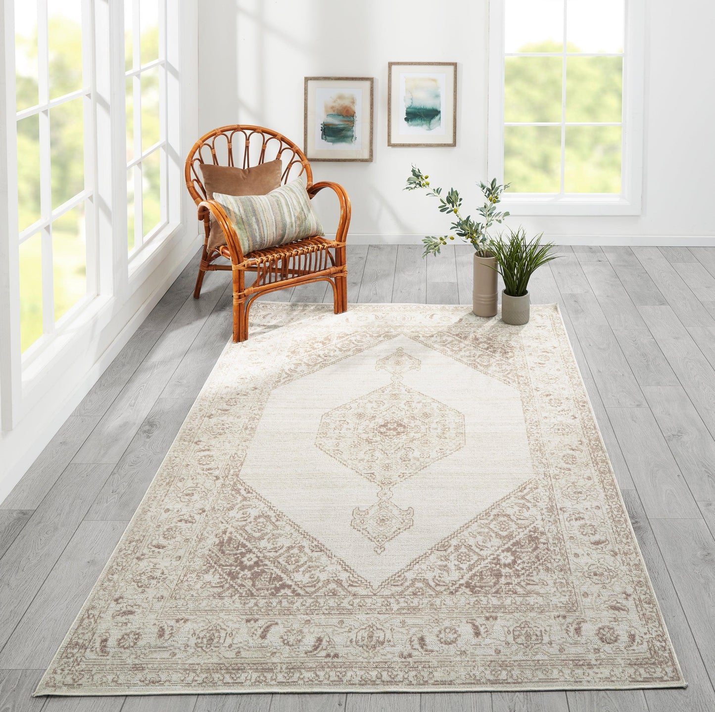 Bright living room with a beige medallion area rug, rattan chair, striped cushion, potted plants & framed wall art.