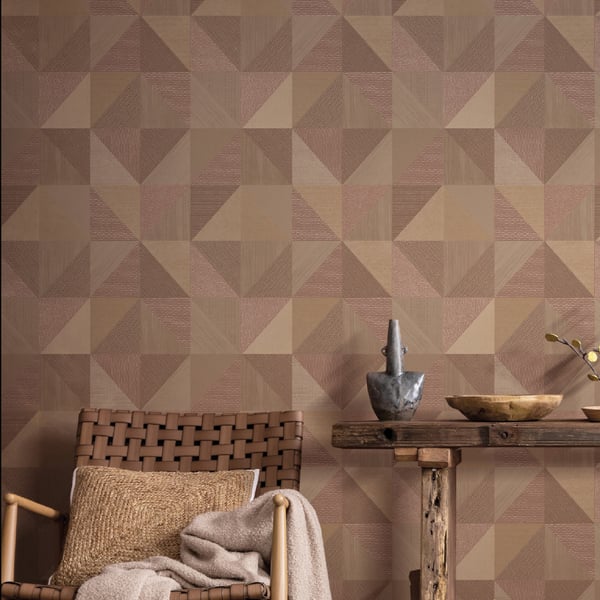 Warm brown geometric triangle wallpaper with woven rattan chair, beige cushion, throw blanket, and rustic wood console.