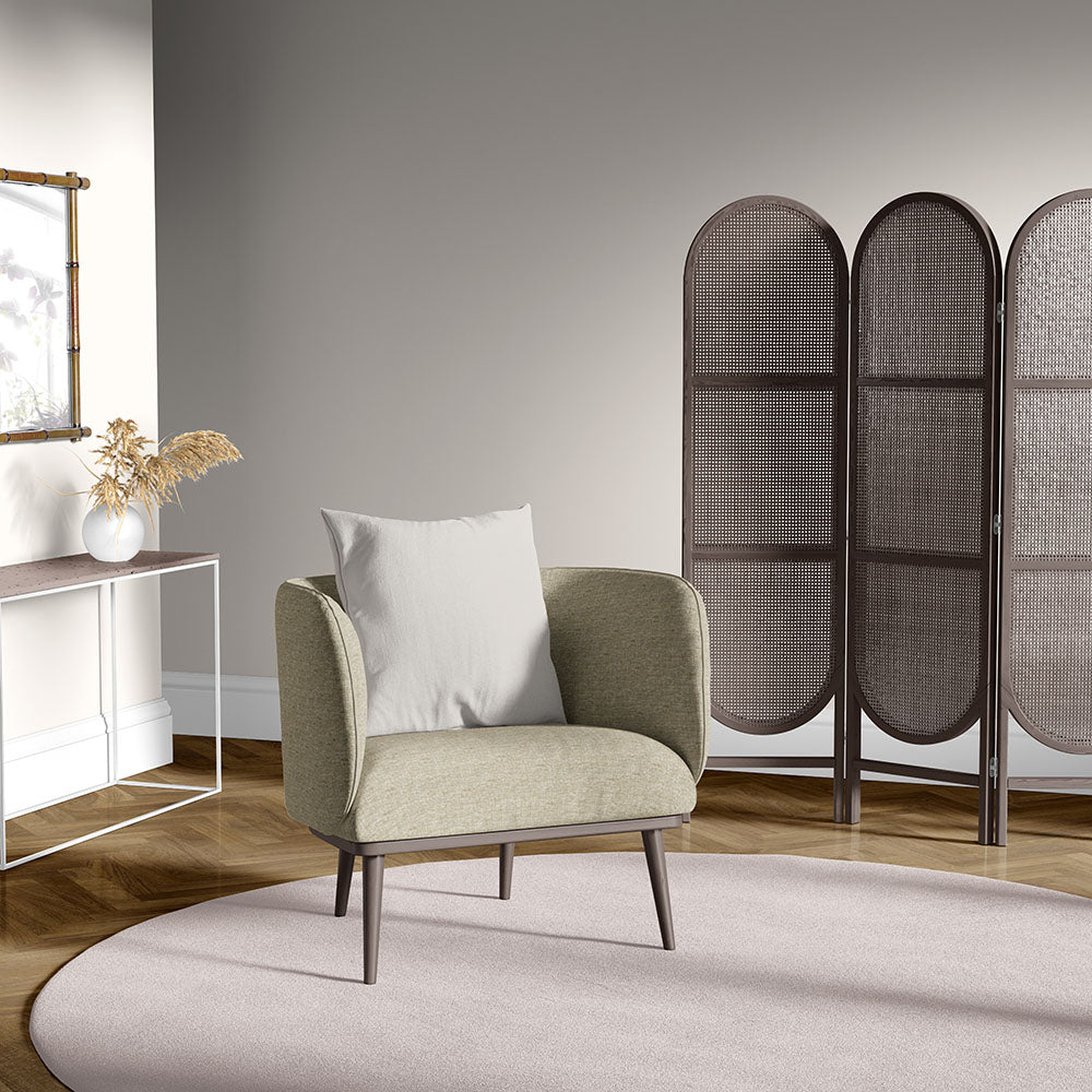 Olive green fabric armchair with light gray cushion in a modern living room with a pale rug and woven room divider.