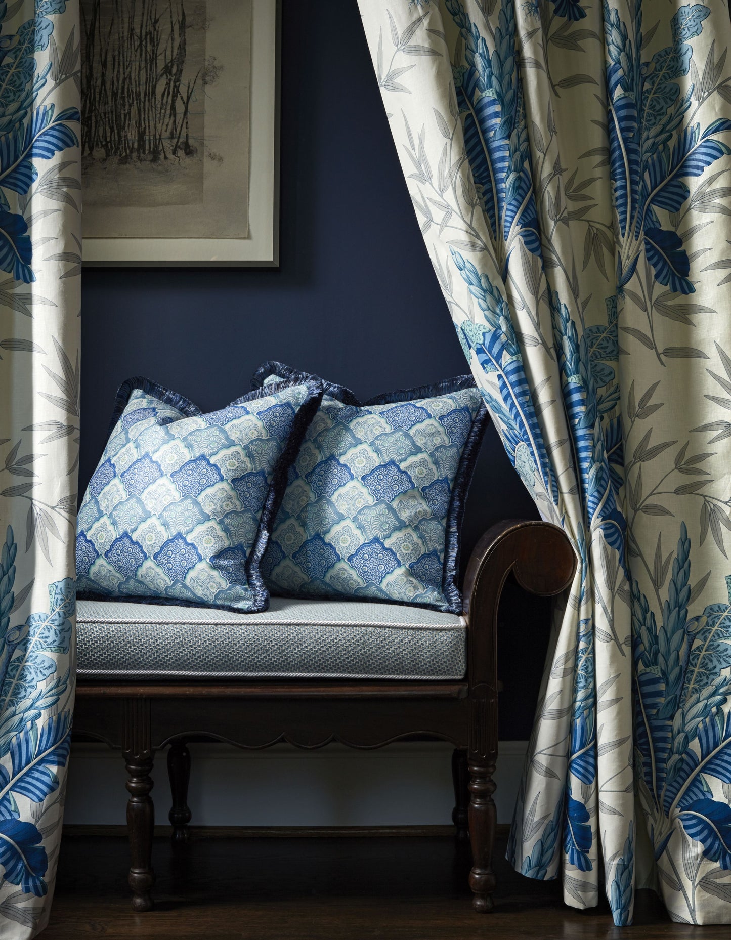 Blue patterned cushions on a dark carved-wood bench, beside curtains with blue botanical prints against a navy wall.