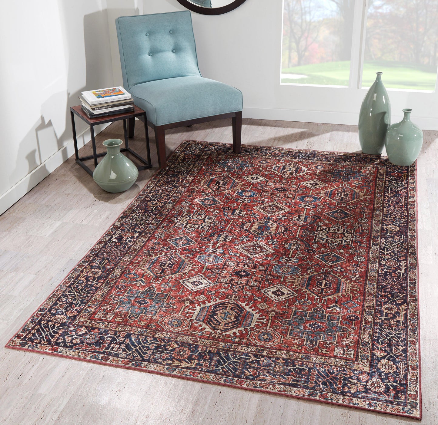 Red and navy Persian-style area rug with intricate pattern on light wood floor, beside a teal chair and green ceramic vases.