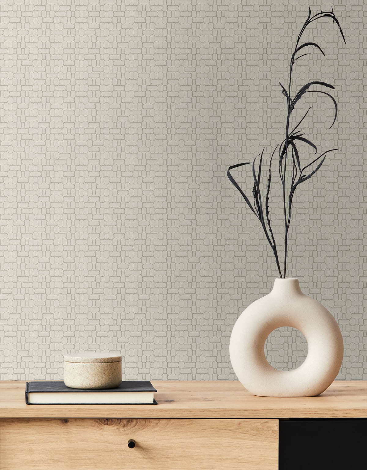 Round hollow ceramic vase with black branch stems on a light wood table, with stacked books and a beige dish.