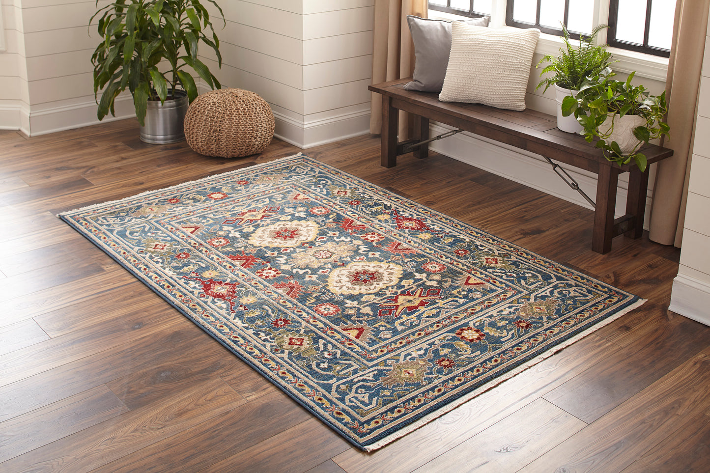 Rectangular blue Persian-inspired area rug with cream, red and gold motifs on a hardwood floor in a bright living room.