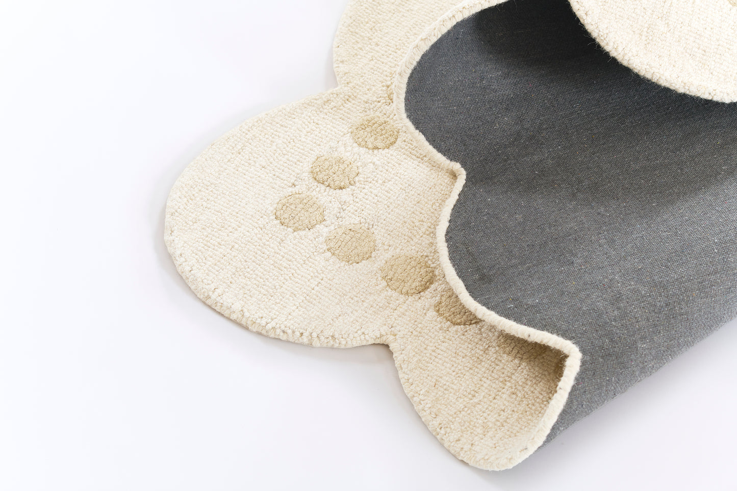 Beige plush rug with scalloped cloud-like edge and circular spots, folded to reveal dark gray underside.