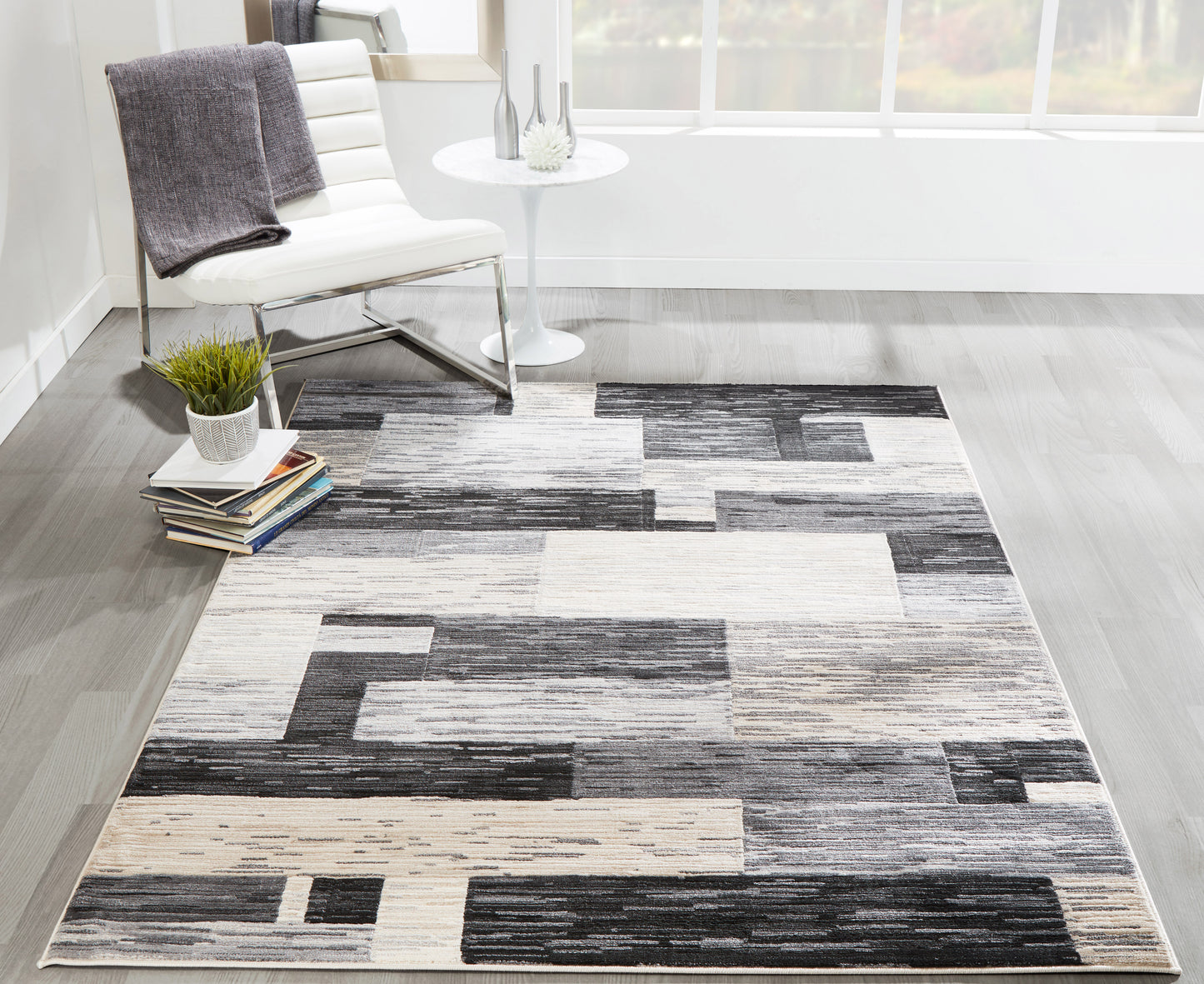 Geometric area rug in grayscale beige blocks; modern living room with white chair and round side table.