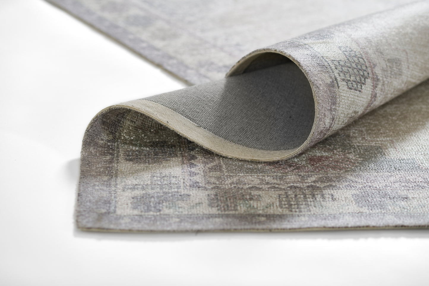 Rolled grey-beige oriental rug with muted floral pattern and soft woven texture.