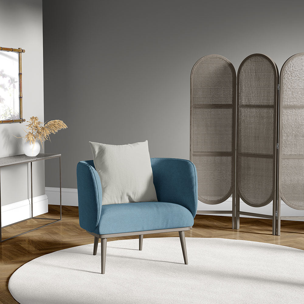 Blue mid-century armchair with cream cushion, tapered legs, in a gray living room with a woven room divider and round rug.