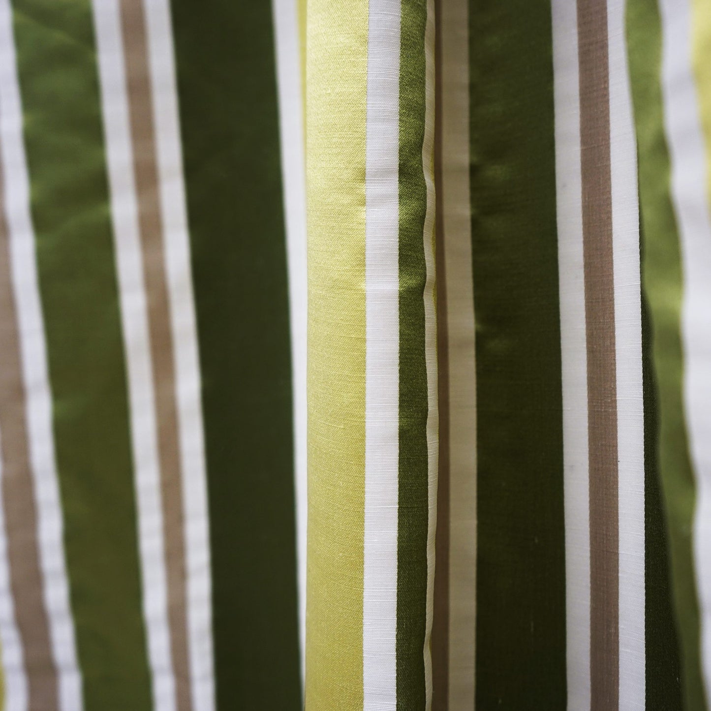 Close-up of striped silk fabric with vertical olive green, lime, white and beige stripes; glossy texture.