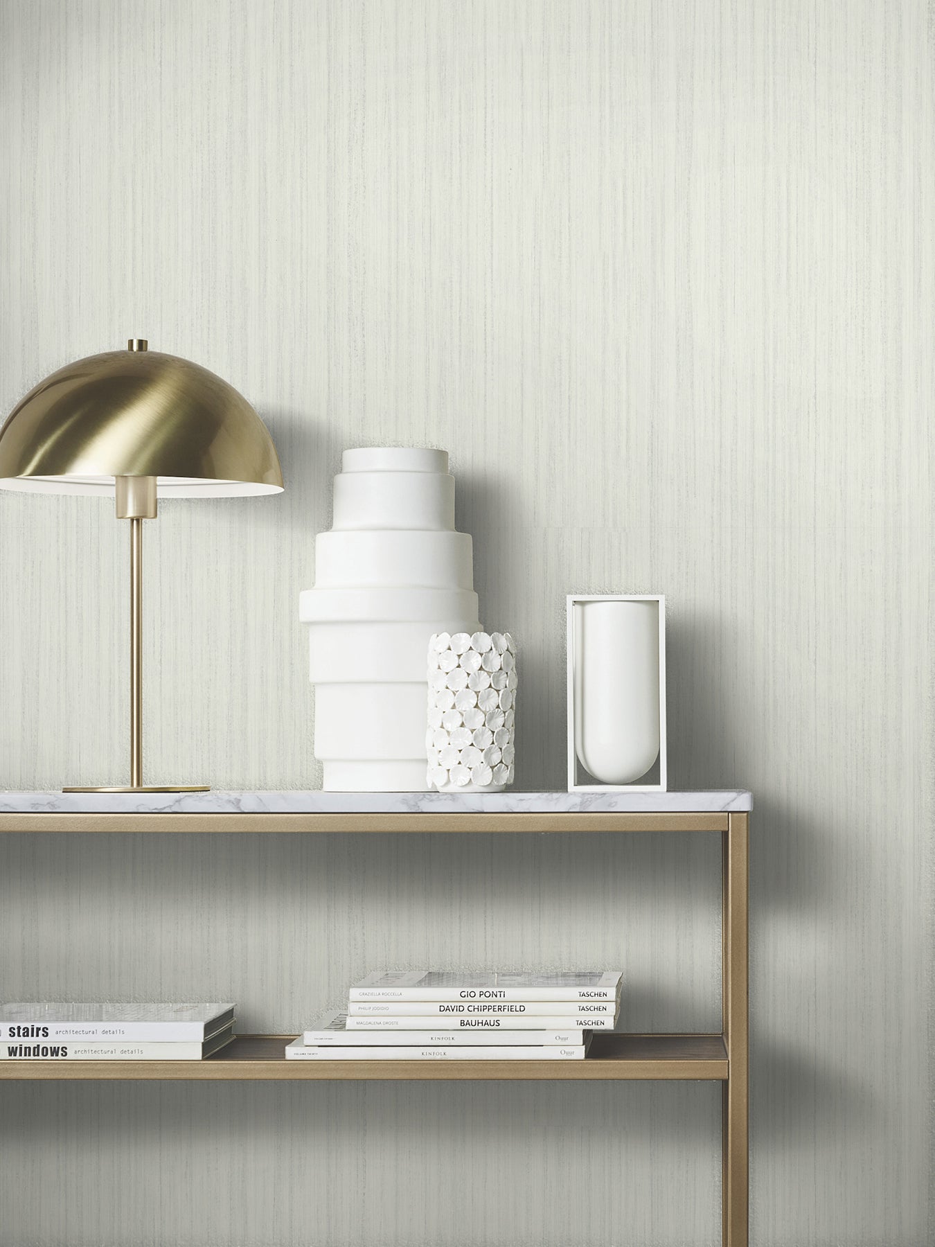 Brass dome table lamp with white ceramic vases on a marble-topped brass shelf, stacked books beneath.