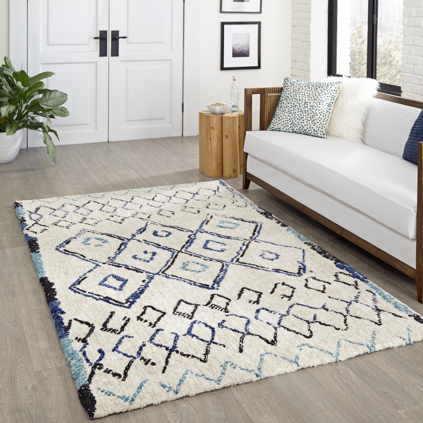 Cream shag area rug with blue geometric diamond pattern and teal border in a modern living room beside a white sofa.