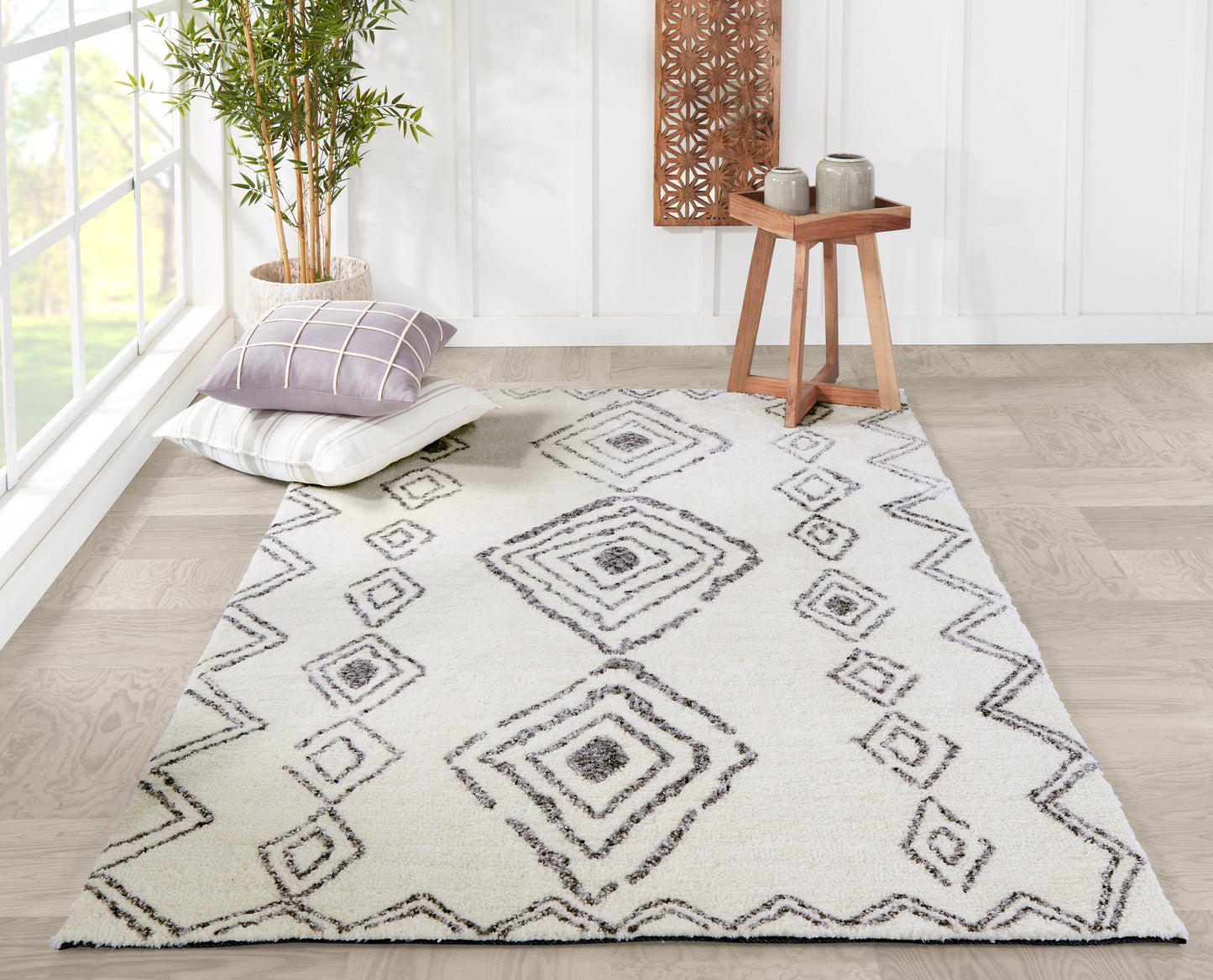 Ivory rug runner with gray diamond pattern and zigzag border; cushions, potted bamboo, and wooden side table in bright room.
