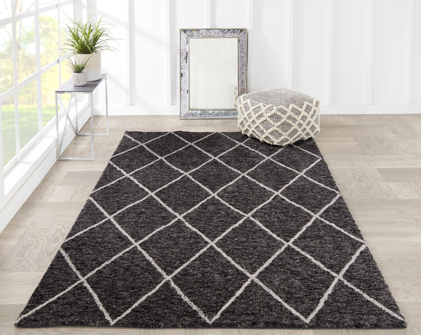 Plush dark gray rug with white diamond lattice, pouf, framed mirror, and plant on metal side table in bright sunlit room.