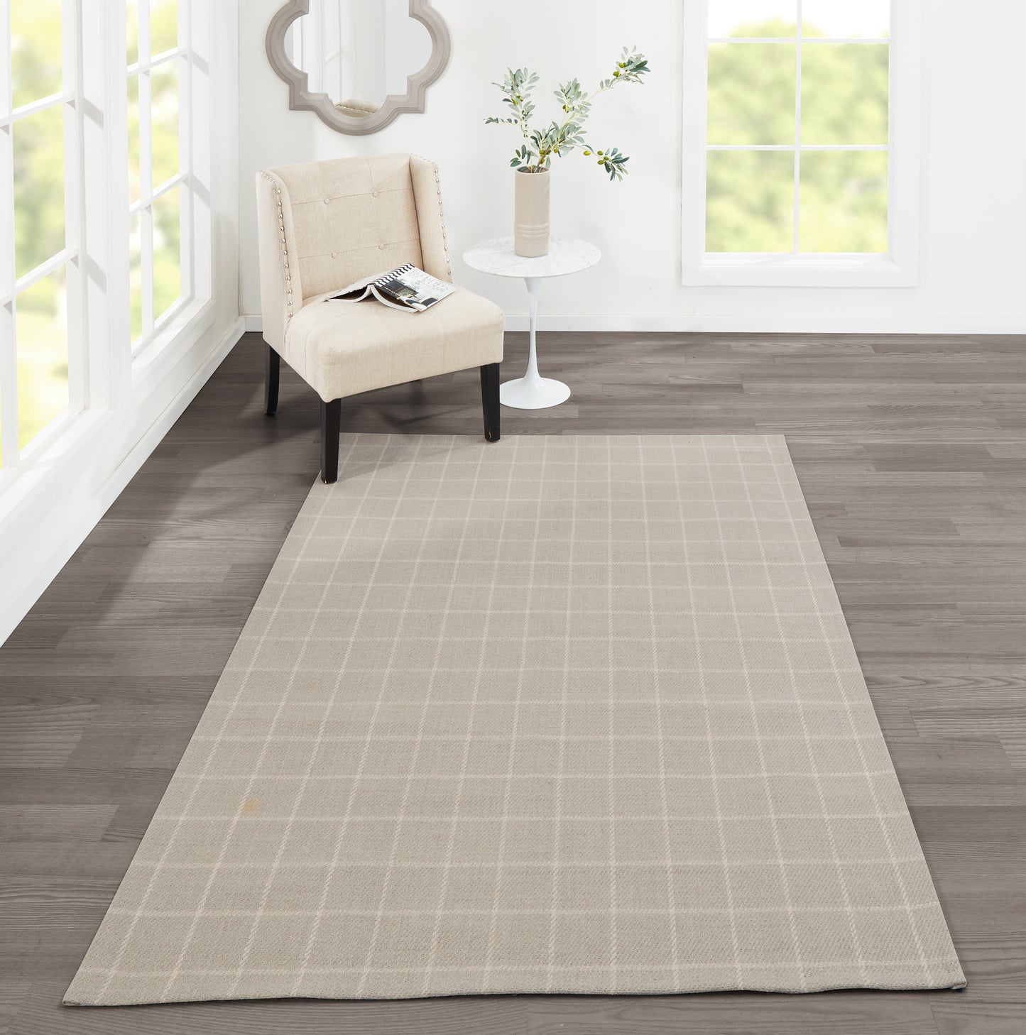 Beige rectangular area rug with a light grid pattern in a bright living room beside a beige chair and white table.